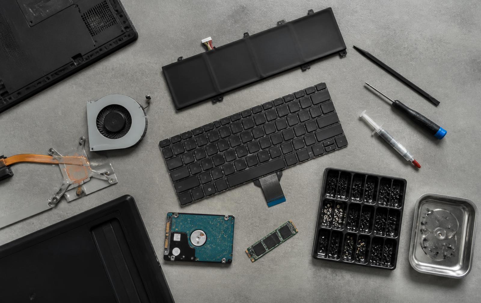 Ersatzteile für Notebooks: Akku, Tastatur, Lüfter, SSD und Schrauben auf einer Werkbank